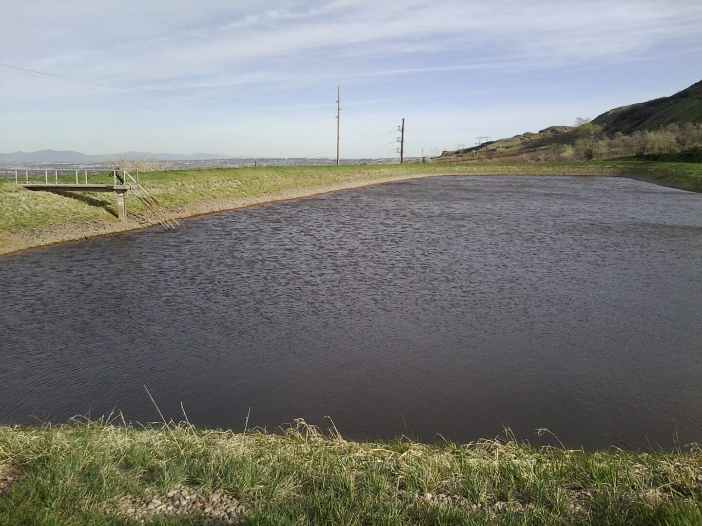 A pond with water running over it and grass on the side.